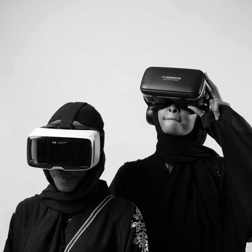 Two women wearing virtual reality headsets in black and white setting.