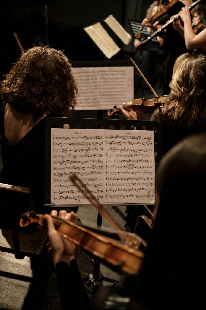 Musicians in an orchestra playing violins during a classical concert with visible musical notes.