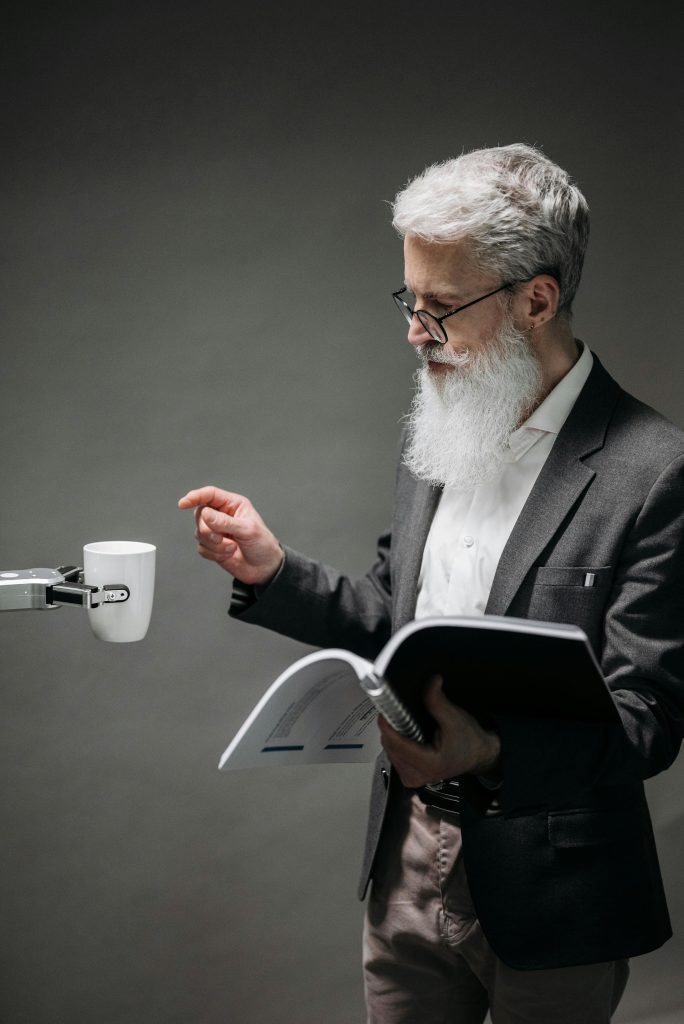 Senior man with gray hair and beard interacts with a robotic arm in a studio setting.